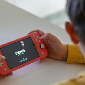 Child holding a pink handheld game console while a digital game loads on the screen.